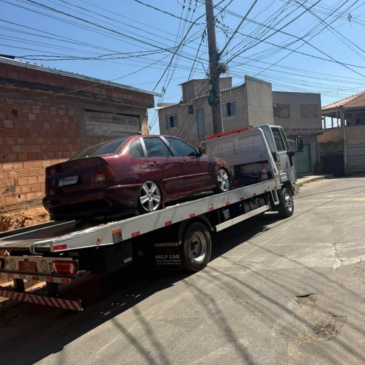 Serviço de reboque transportando carro sedan antigo (vinho) em área urbana.