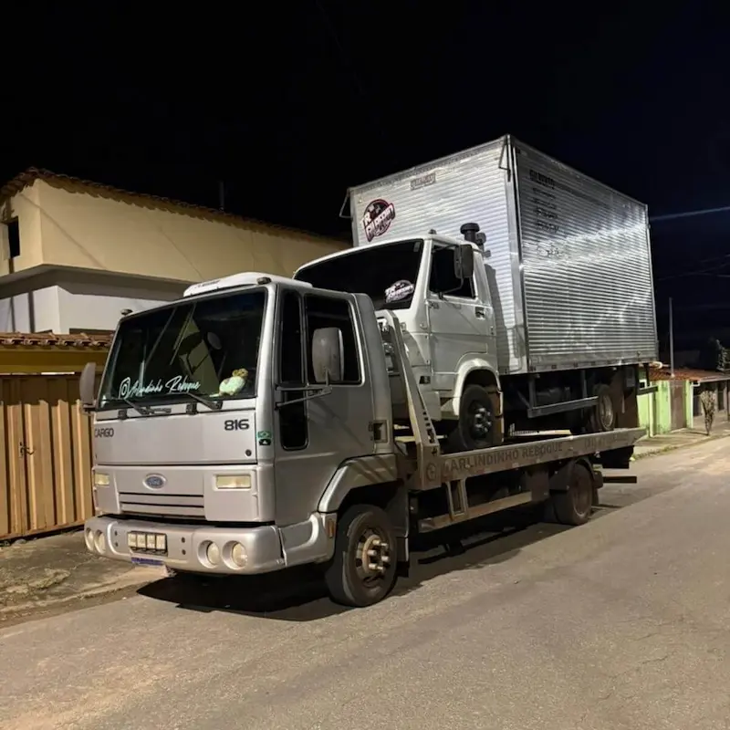 Guincho transportando caminhão baú de pequeno porte (VUC) em área residencial.
