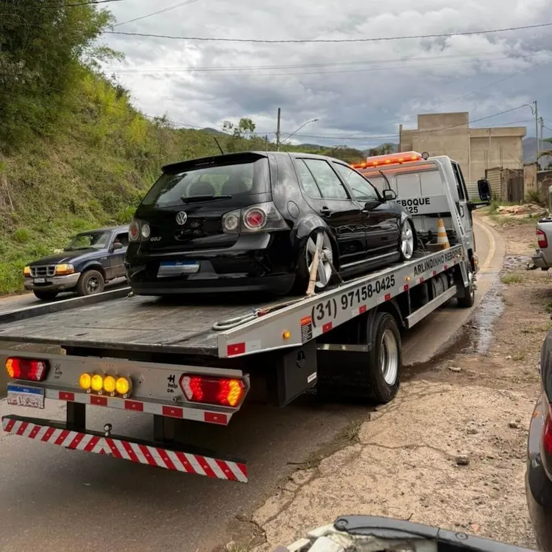 Socorro automotivo transportando carro hatch preto em estrada da região de Mariana.