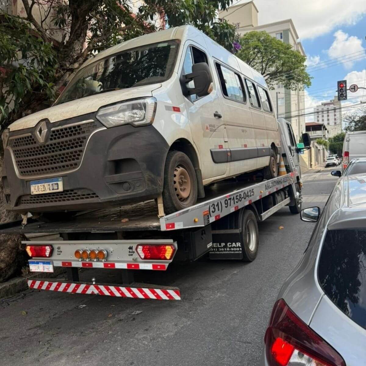 Guincho plataforma transportando van branca avariada para oficina.