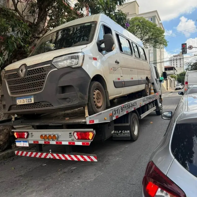 Guincho plataforma transportando van branca avariada para oficina.