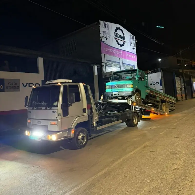 Atendimento noturno de guincho socorrendo caminhão verde em via urbana.